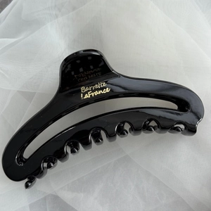 Detail of a large black glossy hair claw with gold Barrette LaFrance text on fabric