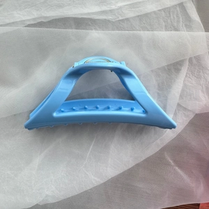Close-up of light blue triangular hair claw clip with non-slip teeth on white fabric
