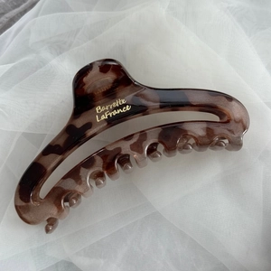 Detailed close-up of large amber leopard print hair claw clip on soft white tulle