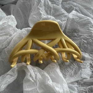 Détail du design tissé croisé sur une pince à cheveux jaune crème sur fond blanc