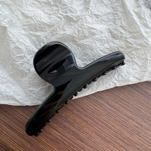 Close-up of a large black glossy hair claw clip with dense teeth on a minimalist background