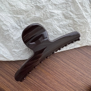 Close-up of large glossy dark brown resin hair claw clip for thick hair styling