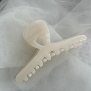 Detail of a cream large hair claw clip with glossy pearlescent finish on soft mesh fabric