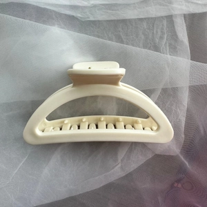 Macro detail of large matte cream hair claw clip with sturdy teeth on white tulle fabric