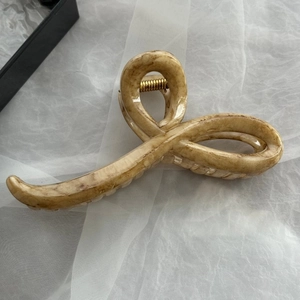 Dettaglio di una grande pinza per capelli in marmo beige con molla dorata