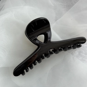 Close-up of a glossy black French hair claw clip on soft white fabric background