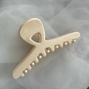 Close-up of a large cream-colored glossy hair claw clip on soft white tulle fabric