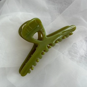 Detail view of olive green glossy hair claw clip on white mesh fabric background