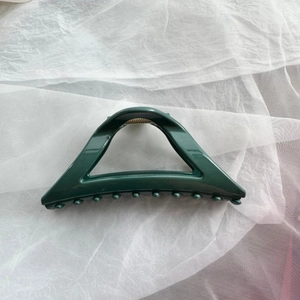 Detail showing deep green triangular hair claw clip with glossy finish on mesh fabric