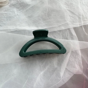 Detail shot of a large forest green silicone shark hair claw clip on white fabric