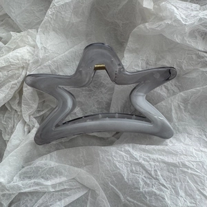 Detail of grey marble star hair claw clip with golden metal spring on white paper