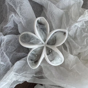 Makroaufnahme der blumenförmigen Haarklammer im weißen Marmor-Design mit Hochglanz-Finish