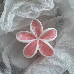 Makroansicht einer Haarspange mit rosa Marmormuster in Blütenform auf weißem Papier