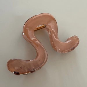 Close-up of translucent amber S-shaped hair claw clip with golden metal spring
