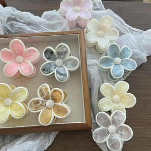 Pinces à cheveux fleurs en acétate aux couleurs de marbre disposées sur un plateau bois