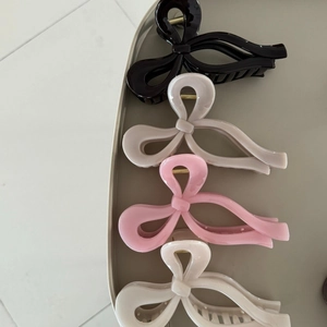 Dettaglio di quattro mollettoni a fiocco in nero, grigio, rosa e crema su un vassoio