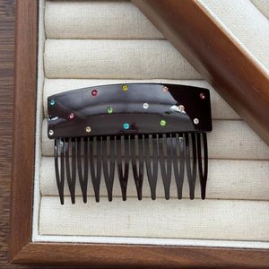 Détail d'un peigne à cheveux marron foncé avec strass colorés sur une boîte en bois