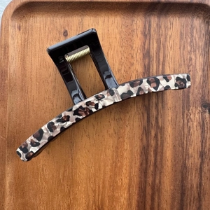 Détail de la pince à cheveux léopard avec ressort doré sur un plateau en bois naturel