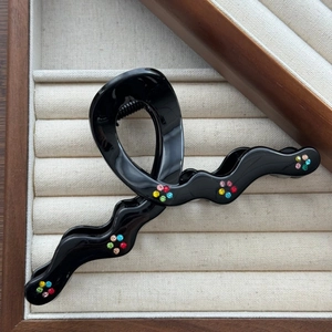 Détail d'une pince à cheveux noire ondulée en résine avec des fleurs en strass colorés