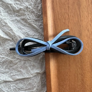 Detail of light blue faux suede bow and glossy black hair clip against wood backdrop