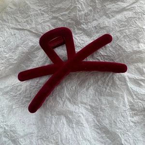 Détail de la pince à cheveux en velours bordeaux avec design croisé sur fond texturé