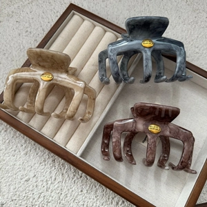 Three large marble pattern shark hair clips in beige, blue, and brown on a wooden tray