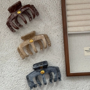 Three large marble pattern shark hair clips with gold relief decor on a wooden tray