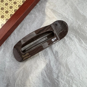 Détail de la pince à cheveux à motif écaille avec logo doré sur fond texturé
