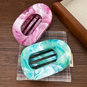 Gros plan de pinces à cheveux en acétate à motif marbre rose et bleu sur un tissu