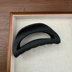 Détail d'une pince à cheveux noire mate en forme de croissant sur plateau beige