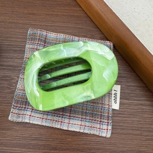 Vue détaillée d'une grande pince à cheveux marbrée verte sur un bureau rétro boisé