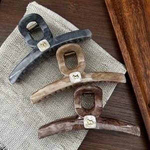 Detailed view of acetate shark hair clips featuring marble textures and golden dog logos