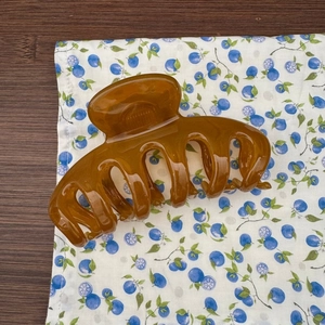 Détail d'une grande pince à cheveux ambrée en acrylique de qualité sur un fond en bois