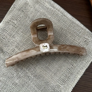Detail of a large marble hair claw clip with golden dog motif on a burlap fabric background