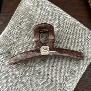 Close-up of marble acetate hair claw clip with golden puppy emblem and white square inlay
