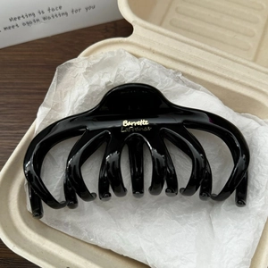 Détail d'une grande pince à cheveux noire brillante avec logo doré dans son coffret