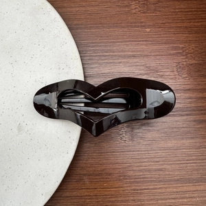 Close-up of a large black heart-shaped hair clip on a minimalist wooden background