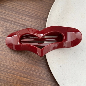 Detailed view of glossy burgundy heart hair clip on a minimalist marble surface