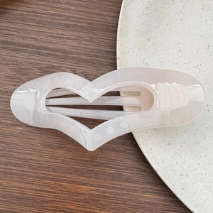 Macro detail of large white marble heart hair clip on a wooden surface and ceramic plate