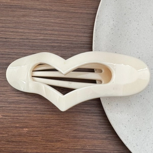Macro detail of cream-colored heart-shaped hair claw clip on a minimalist textured surface