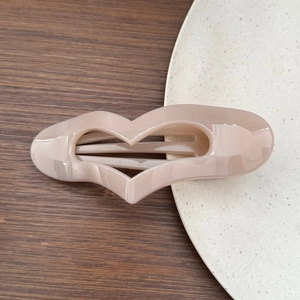 Close-up of a beige heart-shaped hollow hair clip on a minimalist wooden and ceramic base