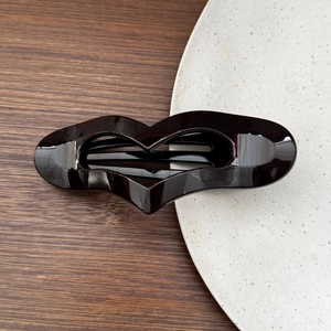 Close-up of a glossy black heart-shaped hair clip on a marble stone surface