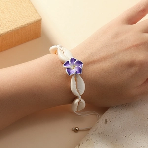 Detail of bohemian shell bracelet with white frangipani flower and braided cord