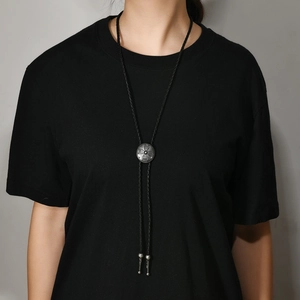 Detail of silver vintage cross bolo tie with black braided cord on a model shirt