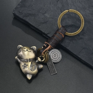 Detail of a bronze Maneki Neko keychain with brown braided leather strap on stone background