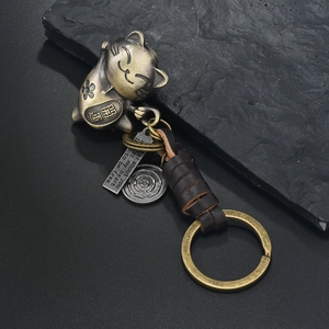 Vintage bronze lucky cat keychain with woven brown leather cord on black stone background
