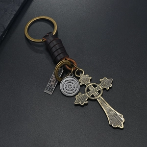 Detail of vintage braided leather keychain with bronze cross and engraved metal charms