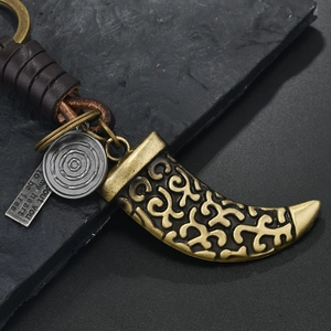 Retro bronze bull horn keychain with woven leather strap on dark stone surface