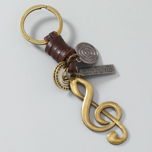 Close-up of vintage bronze music note keychain with leather strap and engraved metal plate