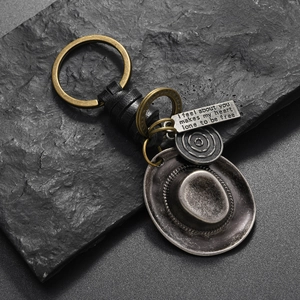 Close-up of vintage cowboy hat keychain with leather strap and engraved metal charms